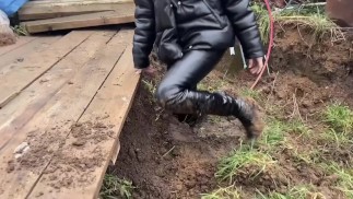 A girl in high-heeled boots likes to get dirty in the mud, she gets her boots dirty up to her knees,